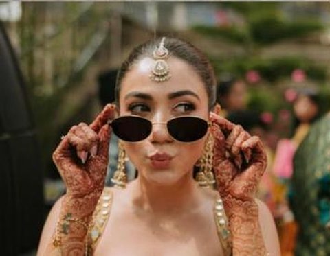 Bride with mehendi hands holding black oval sunglasses