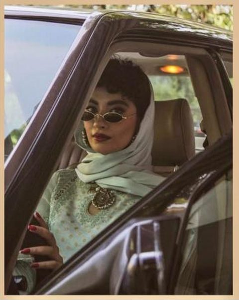 Woman in a pale green outfit wearing small oval sunglasses in a car