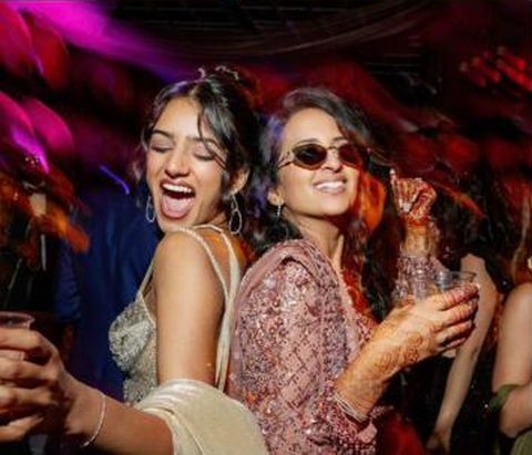 Two women dancing at a sangeet, one in small sunglasses